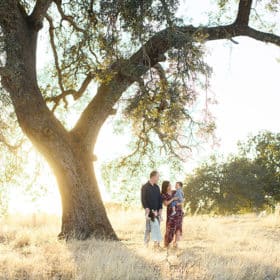 young family standing together under a big oak tree during sunset in sacramento california