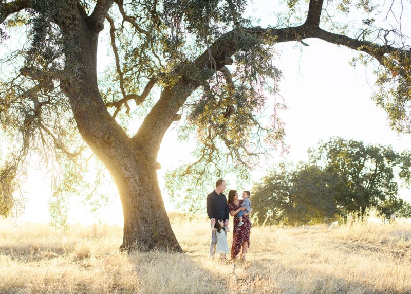 young family standing together under a big oak tree during sunset in sacramento california