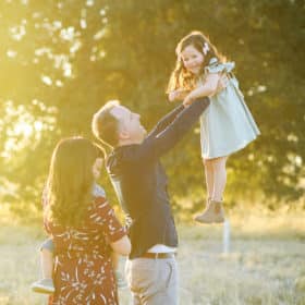 dad holding young daughter up in the air with mom and brother looking on during golden hour fall photos