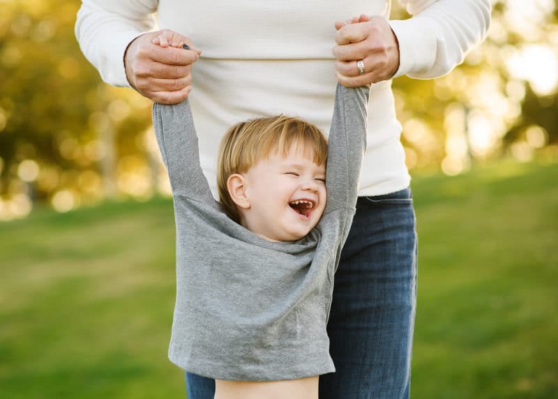 young boy being held up by mom laughing and smiling during fall family photos