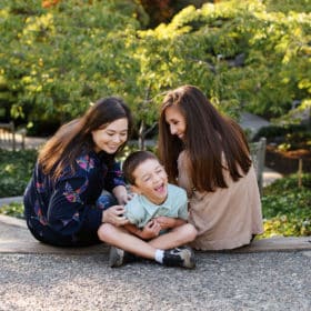 moms with son sitting on the ground and tickling, laughing together during fall family photos