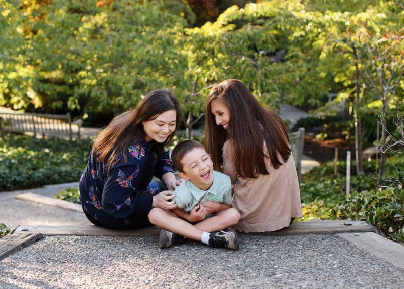 lgbtqia+ moms with son sitting on the ground and tickling, laughing together during fall family photos