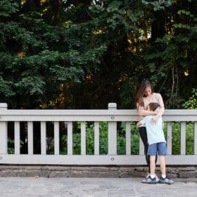 mom hugging young son on a bridge in front of green foliage in berkeley california