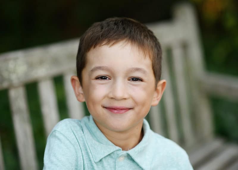 young boy sitting on a bench in berkeley califronia smiling during family photos