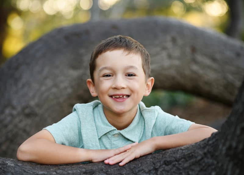 young boy smiling at the camera standing by an oak tree in berkeley california