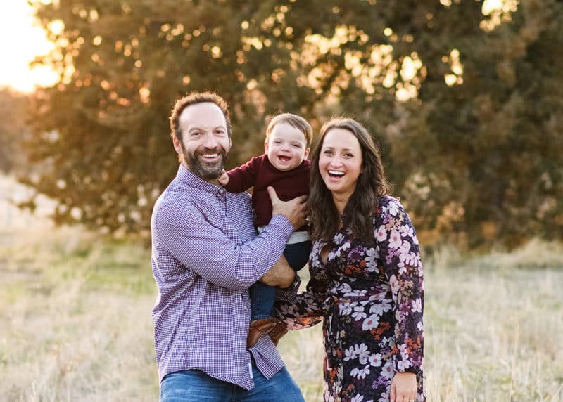 mom and dad holding baby boy and smiling at the camera during fall family photos