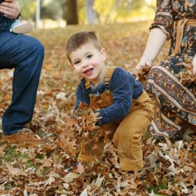 young boy standing in the fall leaves getting ready to throw in the air