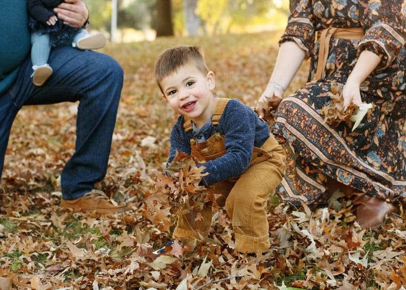 young boy standing in the fall leaves getting ready to throw in the air