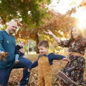 young family throwing fall leaves in the air and laughing during golden hour in fall foliage