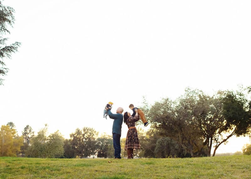 mom holding son, dad holding daughter in the air in a field in golden hour sacramento california