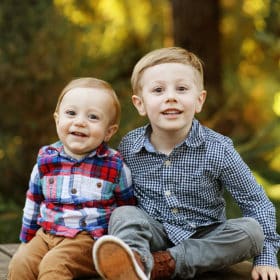 two young brothers sitting on a log smiling at the camera during fall family photos in davis california
