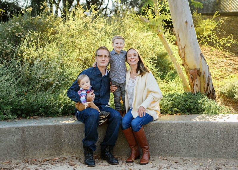 family of four sitting on a bench and smiling at the camera during fall family photos in davis california