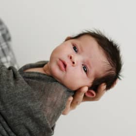 newborn baby boy in dad’s hands looking at the camera during studio session
