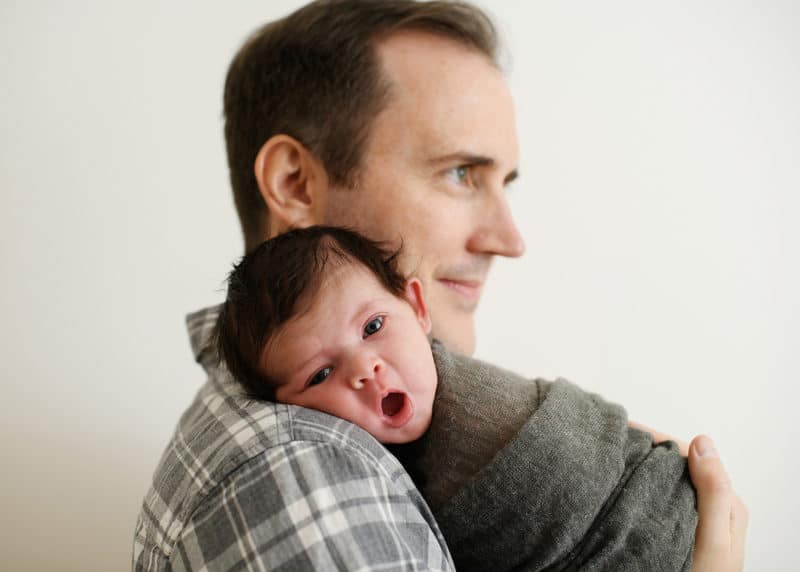 newborn baby boy on dad's shoulder yawning during family studio session