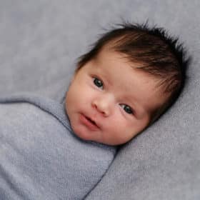 newborn baby boy swaddled in a blanket looking at the camera during studio photo session in sacramento california