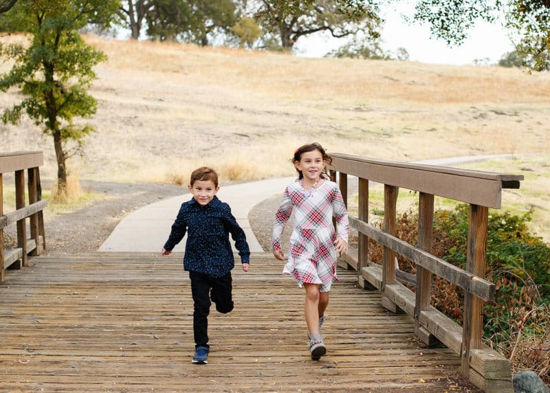 brother and sister running together on a bridge during fall family photos in lincoln california