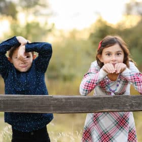 young brother and sister making funny faces along a fence in sacramento california