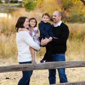 family of four standing by a wooden fence during family photos in lincoln california