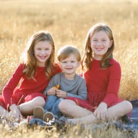 two sisters wearing red dresses with their younger brother sitting in a field