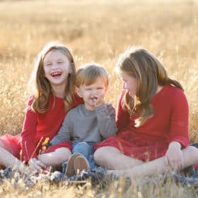 little boy picking his nose during family photos with two older sisters laughing together