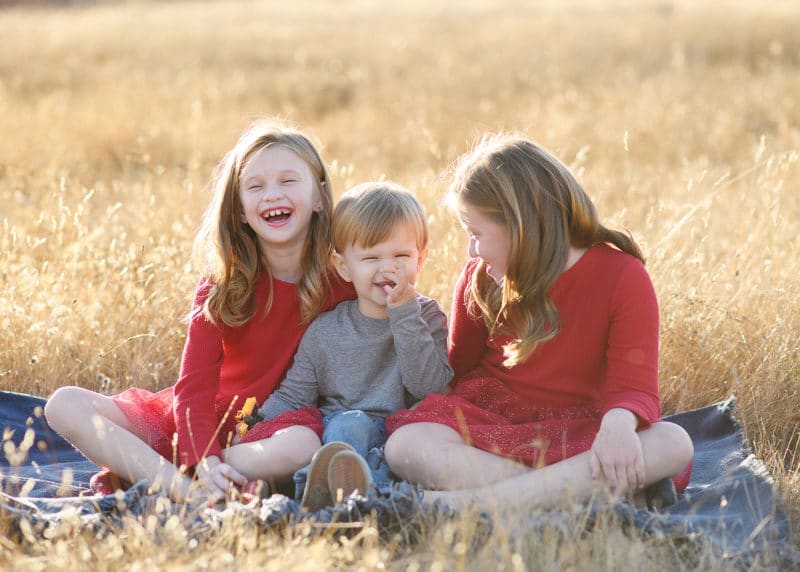 little boy picking his nose during family photos with two older sisters laughing together