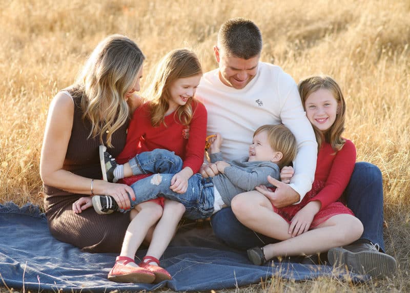 family of five sitting on a blanket in a field looking at one another in sacramento california