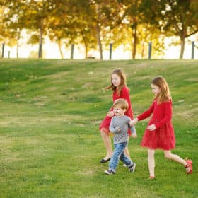 three young siblings running together down a field during family photos in sacramento california