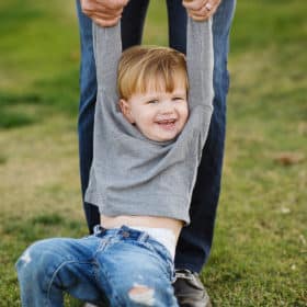 little boy smiling being held by his arms in a grass field during family photos