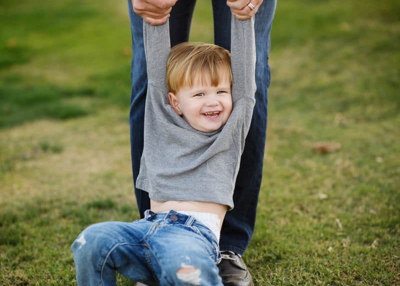 little boy smiling being held by his arms in a grass field during family photos