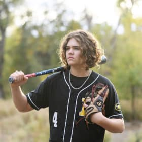 senior in high school boy standing with a baseball bat and glove looking into the distance