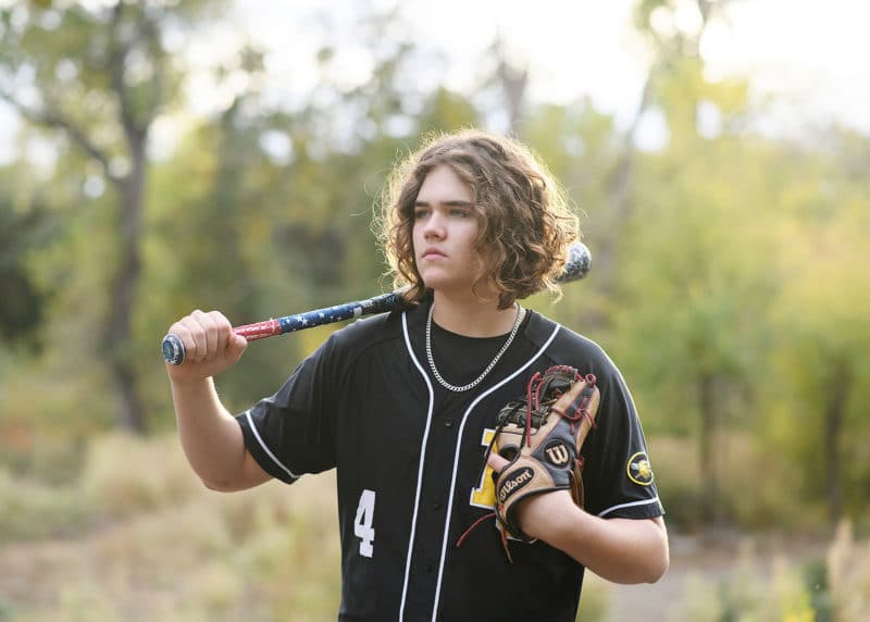 senior in high school boy standing with a baseball bat and glove looking into the distance