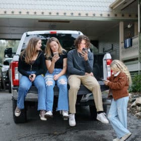 teenage siblings sitting on a truck texting during family photos