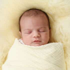 newborn baby swaddled in a blanket laying on a white fur rug during at-home newborn session