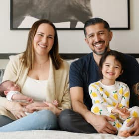 family of four sitting on a bed during at-home newborn session in sacramento california