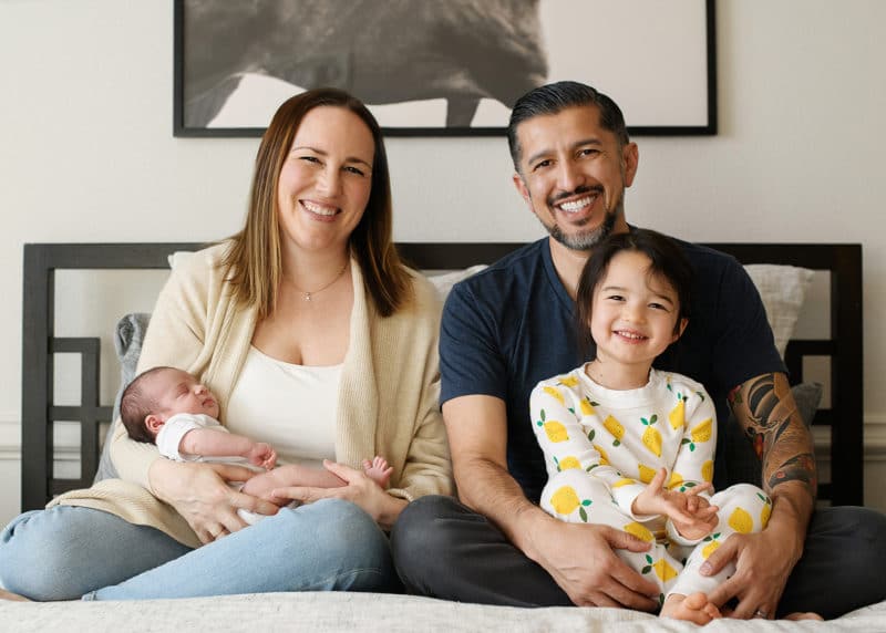 family of four sitting on a bed during at-home newborn session in sacramento california