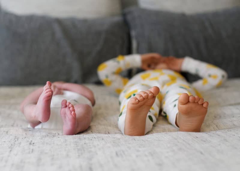 newborn baby with big sister laying on a bed with feet showing