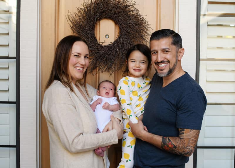 family of four standing outside their front door with newborn baby during at-home photo session in sacramento california