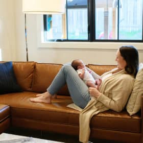 mom sitting on brown leather couch with newborn baby on her lap