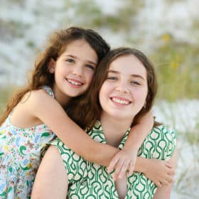 two young sisters sitting on the beach hugging one another during florida vacation