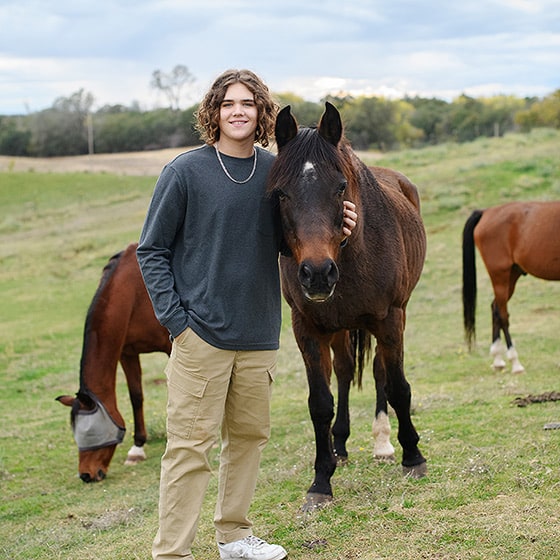 senior boy in high school posing on the family farm with horses during senior session