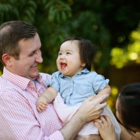 dad holding young daughter and smiling together during a backyard photo shoot