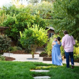 mom and dad holding hands walking in the garden while toddler girl looks behind