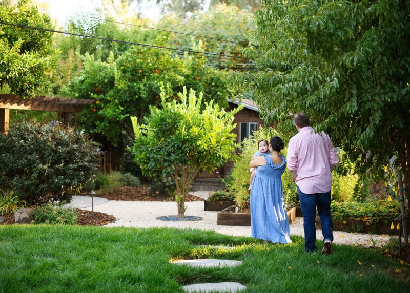 mom and dad holding hands walking in the garden while toddler girl looks behind