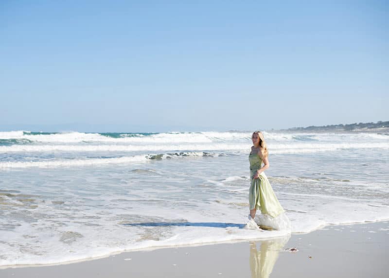 senior in college walking along the beach in a green dress in carmel california