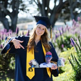 senior in college wearing graduation hat and robe and posing with picture of her brother