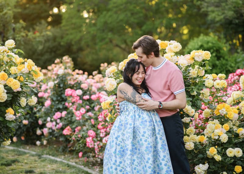 pregnant couple hugging together and laughing in a rose garden during spring in sacramento california