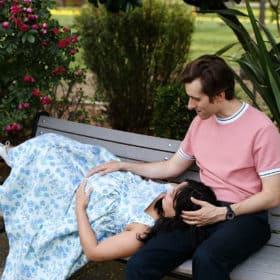 couple sitting on a bench with pregnant woman laying on man’s lap