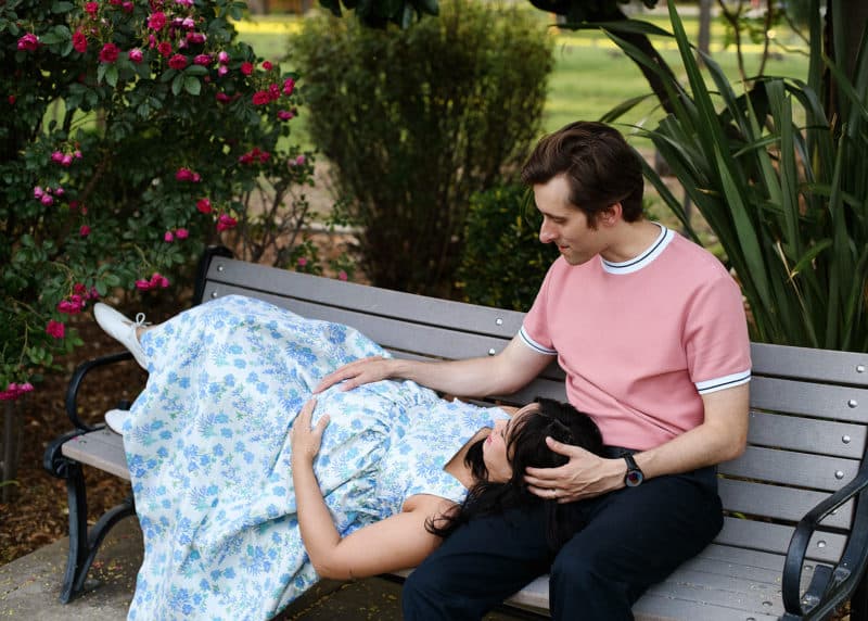 couple sitting on a bench with pregnant woman laying on man's lap