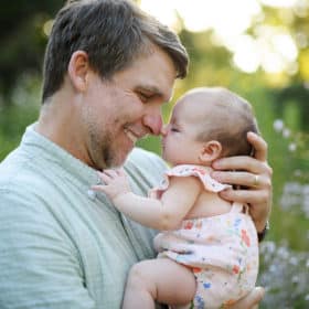 dad holding newborn baby girl in a field of flowers during family photos in sacramento california