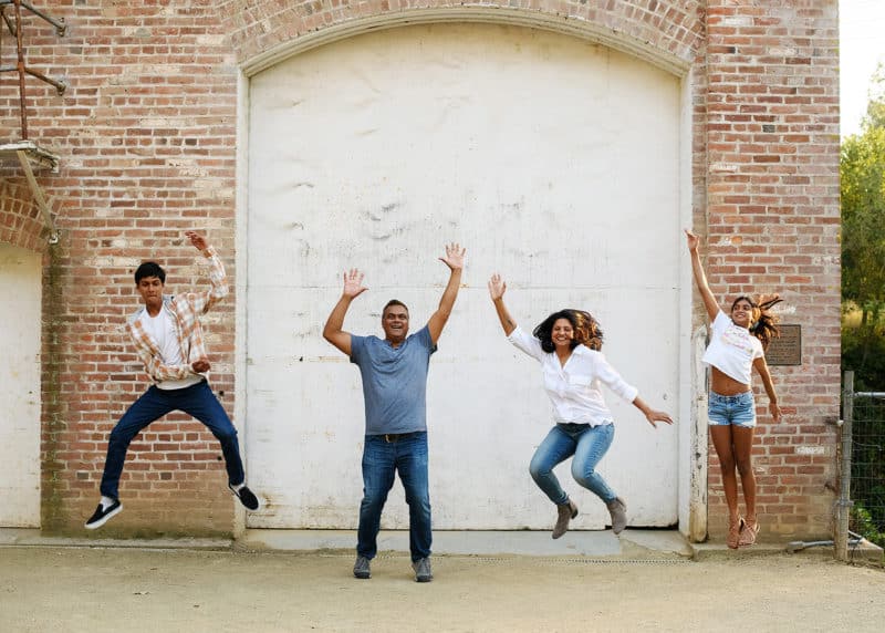 family of four jumping up and down in front of a brick wall during spring family photos